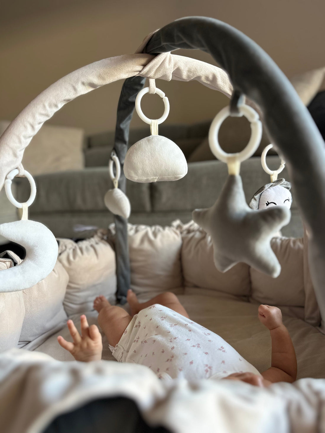 Baby lying on a cocoon style play mat playing with hanging toy mobile