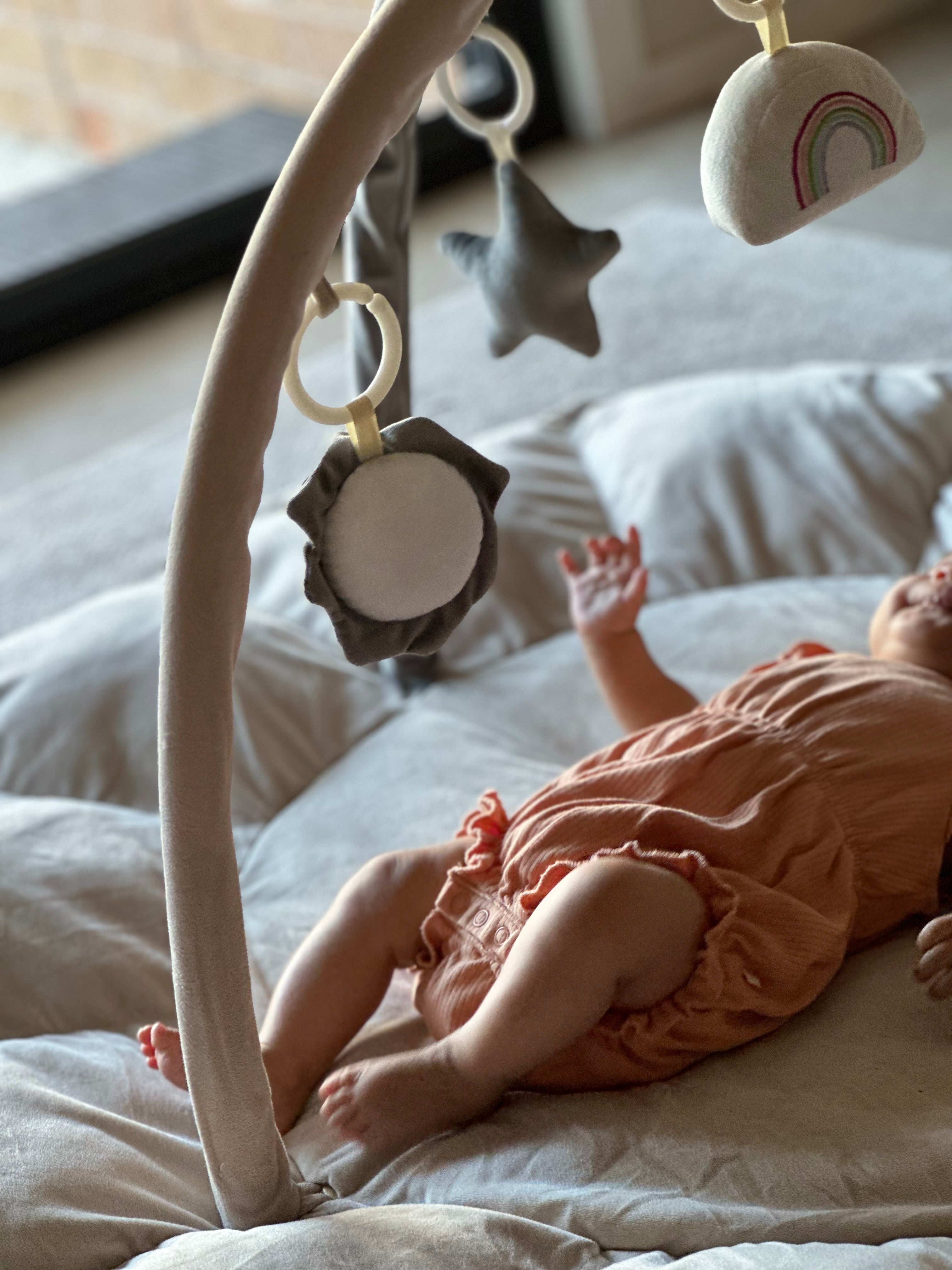 Baby lying on a Lumee Novi play gym playing with toy mobile